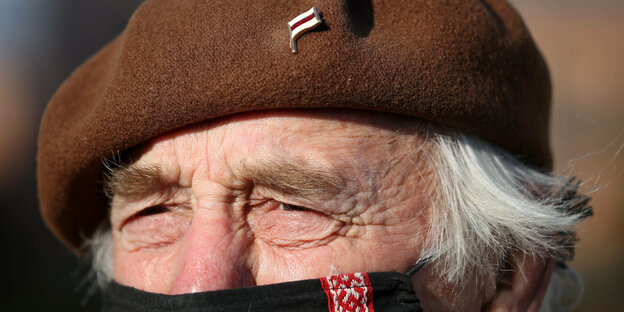 An der braunen Baskenmütze eines äteren Herren hängt eine kleine belerussische Flagge als Anstecker - der Mand trägt Mund-Nasenshutz
