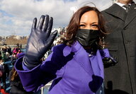 Kamala Harris im violetten Mantel, mit Maske und Handschuhen winkt in die Kamera