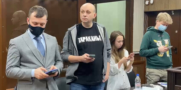 Sergej Smirnow mit zwei jugendlichen Kindern und einem weiteren Mann in einem Gerichtssaal - alle haben ein Smartphone in der Hand