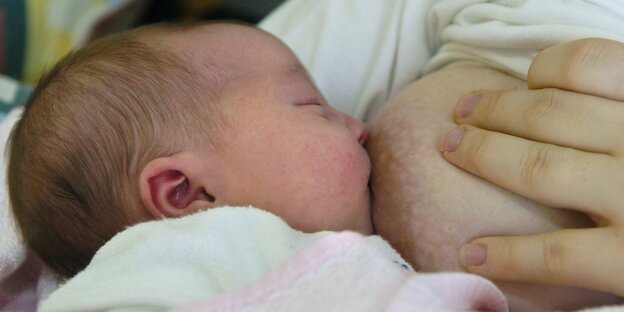 Hier sehen wir ein Baby, das gestillt wird. Es saugt an einer Brust.