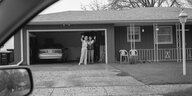 Ein älteres Paar winkt vor der Garage stehend