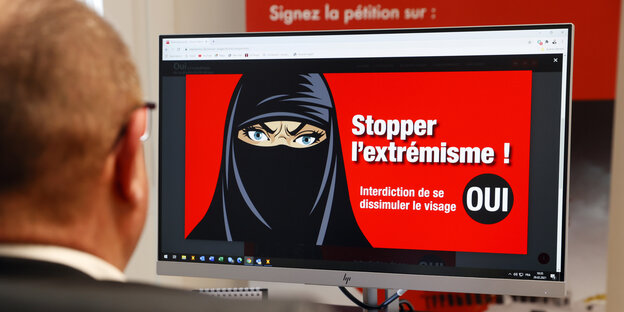 Ein Mann starrt auf einen Bildschirm, auf dem eine Frau mit Gesichtsschleier abgebildet ist. Stoppt Extremismus, steht daneben