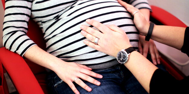 Hebamme hält ihre Hände auf den Bauch einer Schwangeren. Hebamme hält ihre Hände auf den Bauch einer Schwangeren.