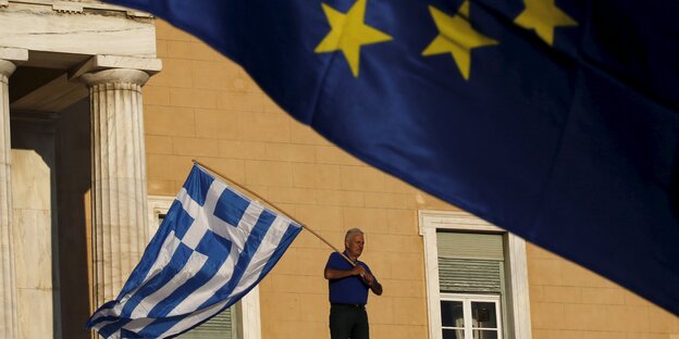 Ein Mann schwenkt eine griechische Flagge, im Vordergrund weht eine europäische Flagge. Ein Mann schwenkt eine griechische Flagge, im Vordergrund weht eine europäische Flagge.