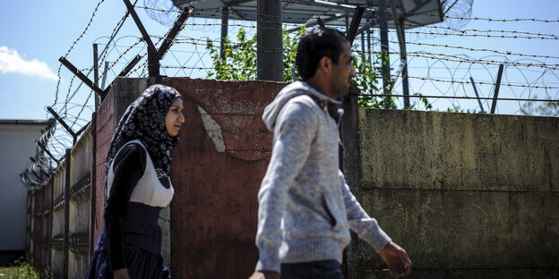 Zwei Flüchtlinge laufen an einer Mauer entlang Zwei Flüchtlinge laufen an einer Mauer entlang