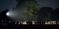 Ein Flutlicht strahlt in einen dunklen Park, im Licht sind viele Menschen zu sehen