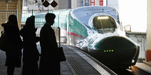 Die Silhouetten von drei Personen an einem Bahnsteig auf welchem gerade ein moderner mintgrüner Schnellzug einfährt