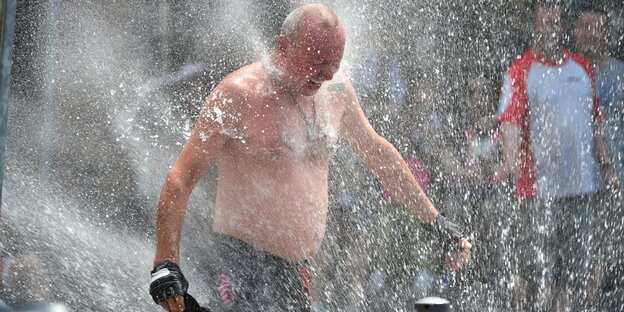 Ein Mensch lässt sich von einem Hydranten nass spritzen