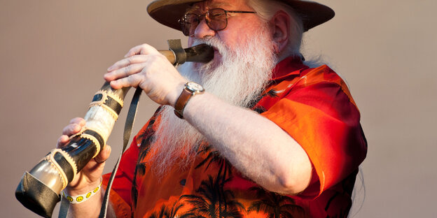 Ein Mann mit weißem Rauschebart bläst in ein brasilianisches Horn Ein Mann mit weißem Rauschebart bläst in ein brasilianisches Horn