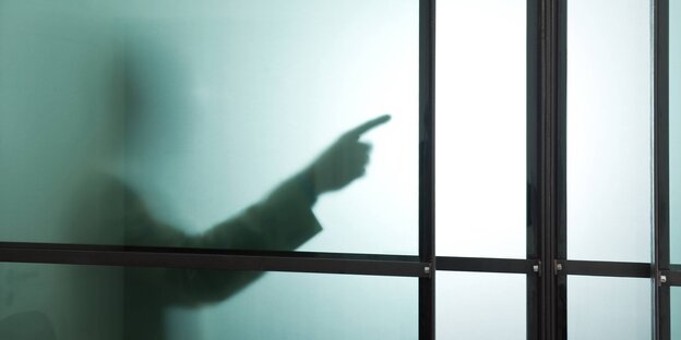 Hinter einer trüben Glaswand gibt eine Hand die Richtung vor Hinter einer trüben Glaswand gibt eine Hand die Richtung vor