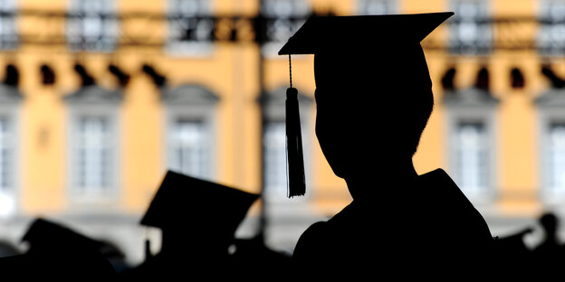 Silhouetten mit Doktorhüten vor Uni-Fassade