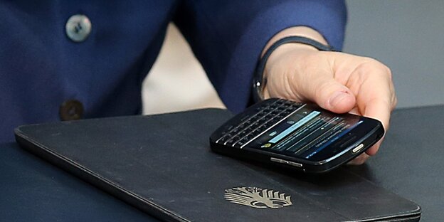 Eine Frau hält ein Smartphone auf einem Ordner mit Bundesadler