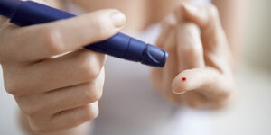 Blutstropfen auf einem Finger, diabetes Meßgerät in der anderen hand