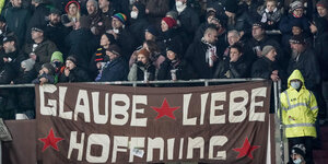 Fußballfans stehen dicht aneinander, im Vordergrund ein Transparent mit den Worten "Glaube, Liebe, Hoffnung"