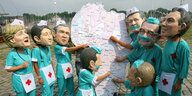 Aktivisten mit Arztkitteln und Regierungschef-Masken zeigen auf eine afrikanische Landkarte.