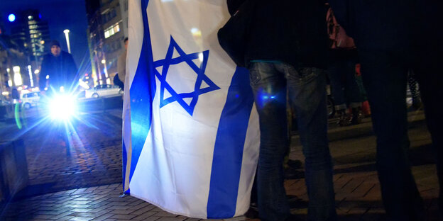 Jemand hält eine Flagge, auf der ein Davidstern zu sehen ist. Jemand hält eine Flagge, auf der ein Davidstern zu sehen ist.