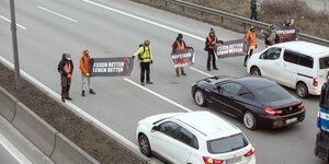 Personen mit Transparenten blockieren eine Autobahn.