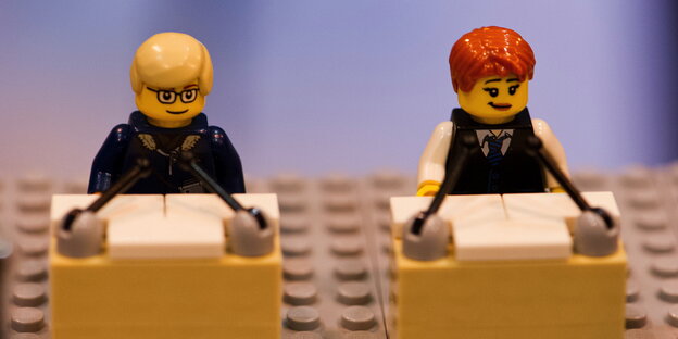 Zwei Legofiguren, die jeweils vor einem Podium stehen. Zwei Legofiguren, die jeweils vor einem Podium stehen.