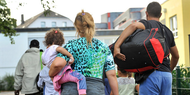 Eine Familie läuft mit Reisetaschen über einen Hof Eine Familie läuft mit Reisetaschen über einen Hof
