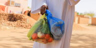 Eine Person in einem weißen Gewand trägt Tüten mit Lebensmitteln, Khartoum, Sudan