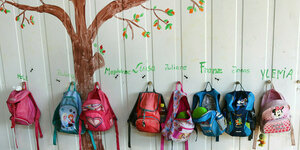 Kinderrucksäcke hängen an einer Wand, auf die ein baum gemalt ist