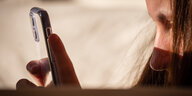 Ein Mädchen hält ein Handy vor ihre Augen, sie ist im Profil zu sehen