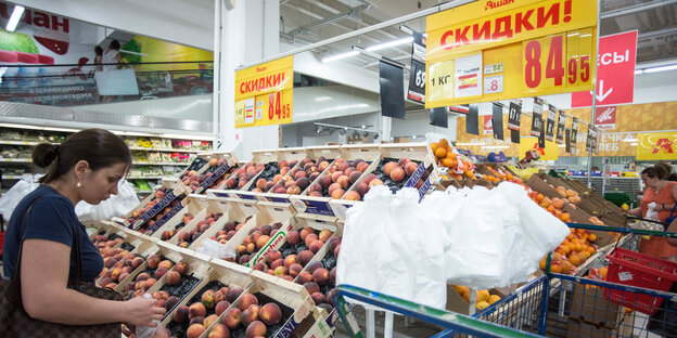 Eine Frau vor Regalen voller Pfirsiche in einem Supermarkt Eine Frau vor Regalen voller Pfirsiche in einem Supermarkt