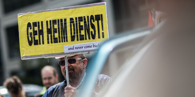 Ein Mann hält ein Schild mit der Aufschrift „Geh Heim Dienst“ Ein Mann hält ein Schild mit der Aufschrift „Geh Heim Dienst“