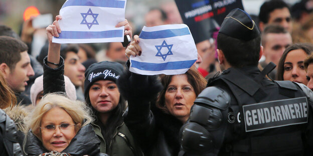 In einer Menschenmenge werden vereinzelt israelische Flaggen hochgehalten. In einer Menschenmenge werden vereinzelt israelische Flaggen hochgehalten.