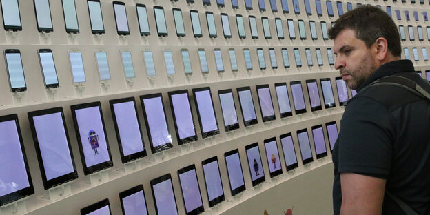 Ein Mann steht vor einer Wand mit vielen Tablet-Computern Ein Mann steht vor einer Wand mit vielen Tablet-Computern