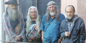 vier ältere Männer mit langen Haaren und lässiger Pose