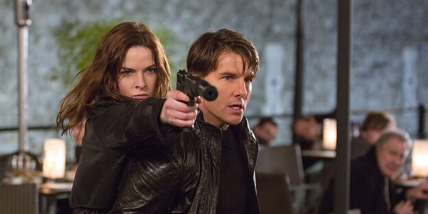 Rebecca Ferguson schießt über die Schulter von Tom Cruise