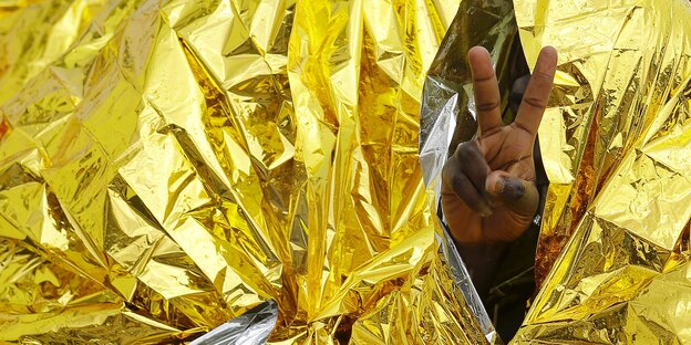 Eine Hand macht das V-Zeichen vor eine Thermodecke Eine Hand macht das V-Zeichen vor eine Thermodecke