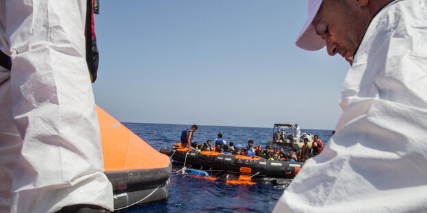 Schlauchboot mit Flüchtlingen im Meer, davor zwei Helfer Schlauchboot mit Flüchtlingen im Meer, davor zwei Helfer