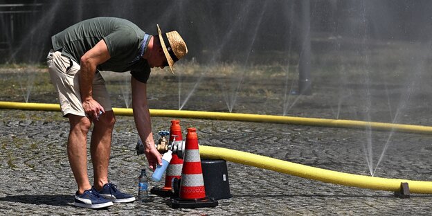 Ein mann füllt eine Wasserflasche mit Wasser an einem Schlauch an der Straße
