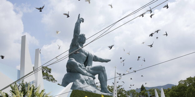 Denkmal eines auf den Himmel zeigenden Menschen, Tauben flattern drum herum Denkmal eines auf den Himmel zeigenden Menschen, Tauben flattern drum herum