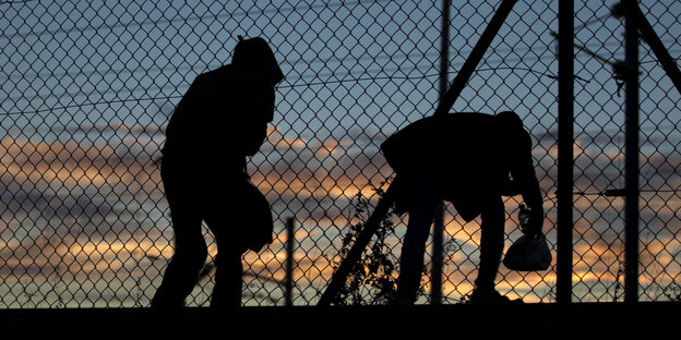 Zwei Flüchtlinge überqueren einen Zaun in der Dunkelheit. Zwei Flüchtlinge überqueren einen Zaun in der Dunkelheit.