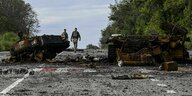 Zerstörte russische Militärfahrzeuge verunreinigen eine Landstraße - im Hintergrund entfernen sich zwei Soldaten