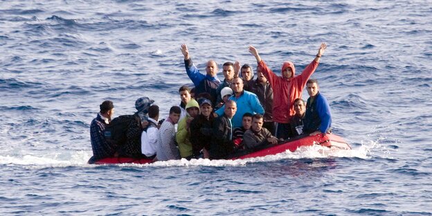 Ein kleines Boot mit vielen Männern an Bord, von denen einige die Arme in die Luft recken Ein kleines Boot mit vielen Männern an Bord, von denen einige die Arme in die Luft recken