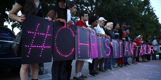 Menschen halten leuchtende Schilder, die zusammen „#CHRISTIAN TAYLOR“ ergeben Menschen halten leuchtende Schilder, die zusammen „#CHRISTIAN TAYLOR“ ergeben