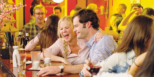 HauptdarstellerInnen Amy Schumer und Bill Hader sitzen an einer Bar und lachen, sie hat einen Arm um seine Schulter gelegt HauptdarstellerInnen Amy Schumer und Bill Hader sitzen an einer Bar und lachen, sie hat einen Arm um seine Schulter gelegt