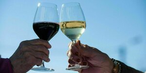 Ein Mann und ein Frau halten je ein Rotwein- und ein Weißweinglas in der Hand - die Gläser sind halbvoll
