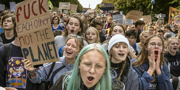 Eine große Masse rufender Schüler*innen, eine von ihnen hält ein Schild, auf dem steht "fuck each other, not the planet"