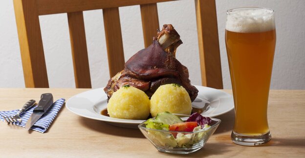 Ein Teller mit Schweinshaxe und Klößen. Ein Weizenbier rechts vom Teller. Besteck links vom Teller. Davor ein kleiner gemischter Salat. Ein Teller mit Schweinshaxe und Klößen. Ein Weizenbier rechts vom Teller. Besteck links vom Teller. Davor ein kleiner gemischter Salat.