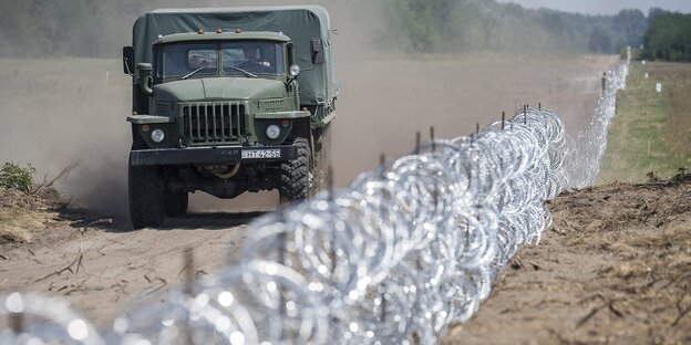 Militärlastwagen fährt den Stacheldrahtzaun an der Grenze entlang Militärlastwagen fährt den Stacheldrahtzaun an der Grenze entlang