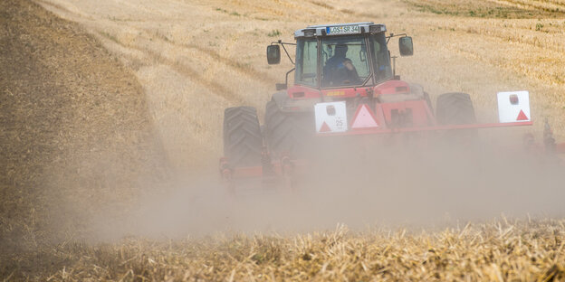 Eine Traktor fährt auf einem Kornfeld und ist von Staub umgeben Eine Traktor fährt auf einem Kornfeld und ist von Staub umgeben