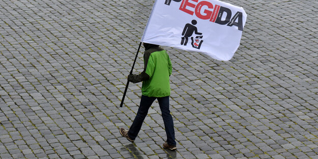 Mann mit Pegida-Fahne läuft über leeren Platz Mann mit Pegida-Fahne läuft über leeren Platz