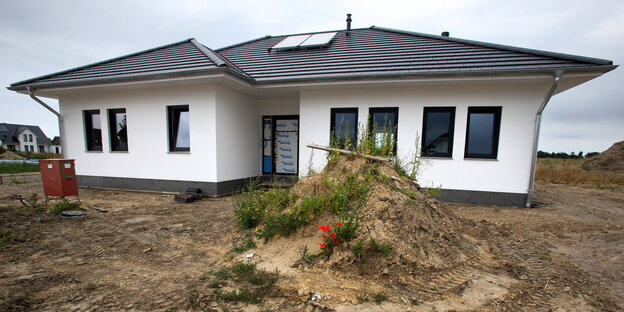 ein anderhalbstöckiges weißes Haus, das gerade gebaut wurde und vor dem ein Hügel mit Bauschutt steht