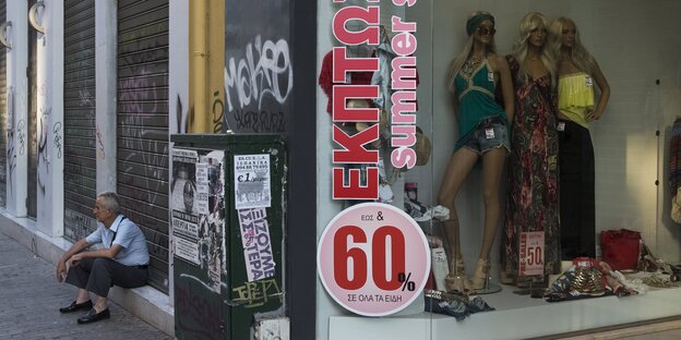 Ein Mann sitzt vor einem Laden der 60 Prozent Rabatt anbietet Ein Mann sitzt vor einem Laden der 60 Prozent Rabatt anbietet
