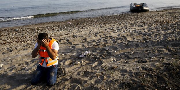 Ein Mann in Schwimmweste am Strand bedeckt sein Gesicht mit den Händen